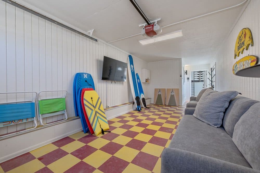 Beach themed garage hangout with sofas, surfboards, and a television